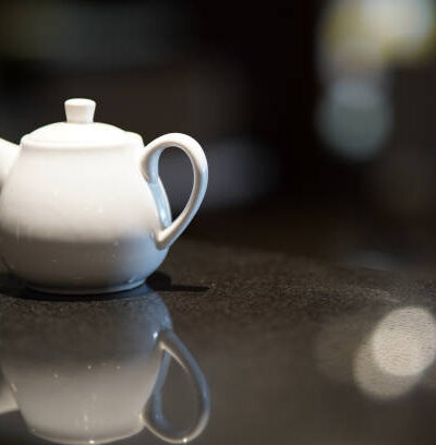 White ceramic teapot for brewing tea on a black background with reflection