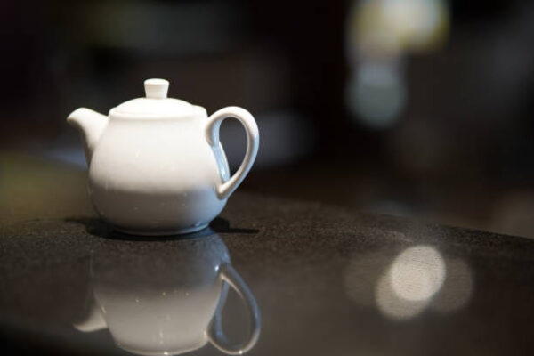 White ceramic teapot for brewing tea on a black background with reflection